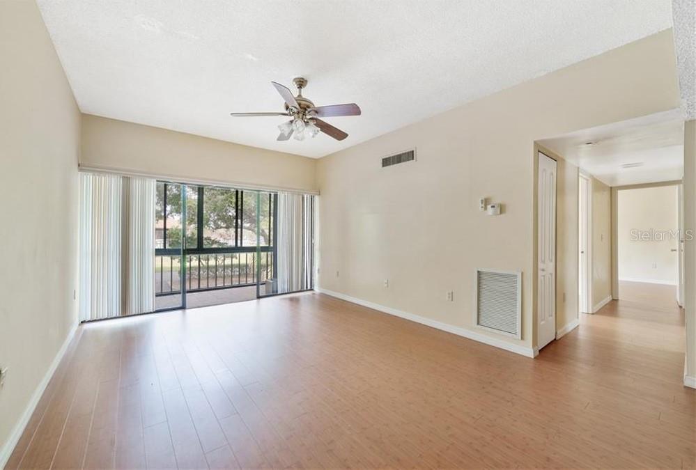 An empty living room with light wood flooring, a ceiling fan, and a sliding glass door — 3254 S SEMORAN BOULEVARD UNIT 21, ORLANDO, FL