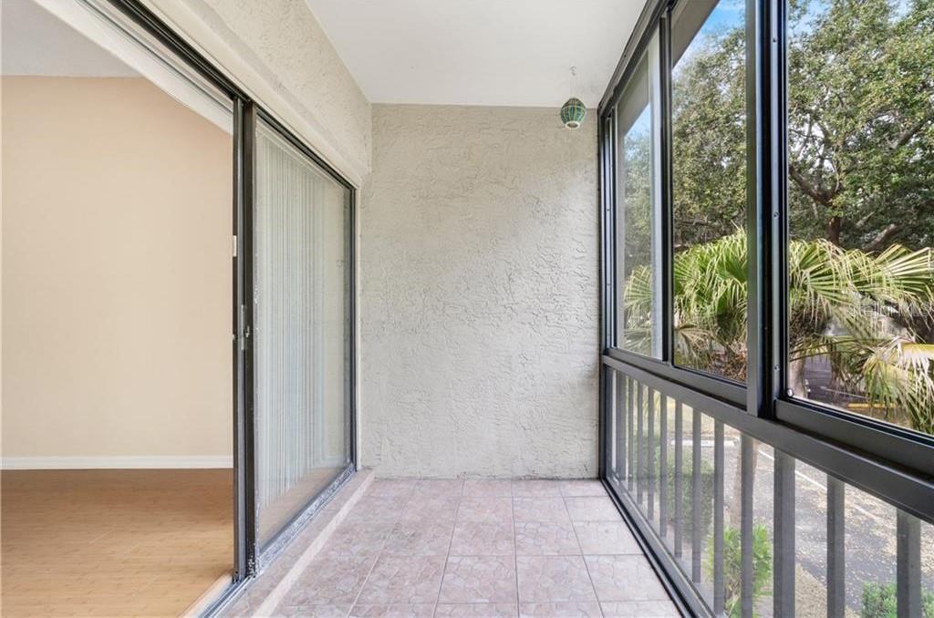 A covered balcony with tiled flooring, a sliding glass door, and large screened windows — 3254 S SEMORAN BOULEVARD UNIT 21, ORLANDO, FL