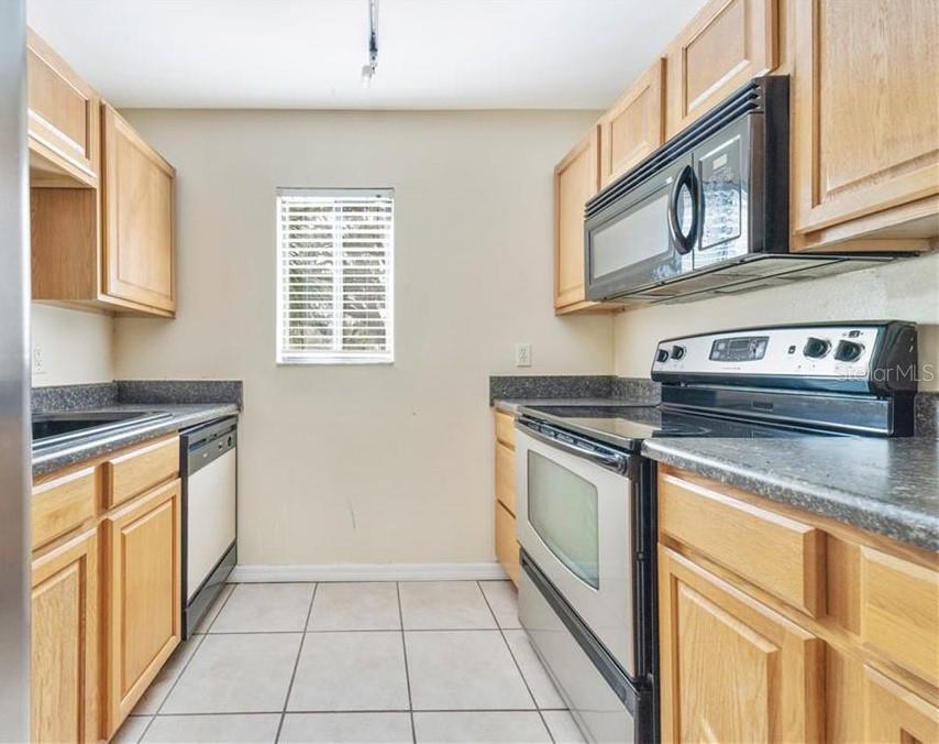A galley kitchen features light wood cabinets, dark countertops, tile flooring, and stainless steel appliances — 3254 S SEMORAN BOULEVARD UNIT 21, ORLANDO, FL