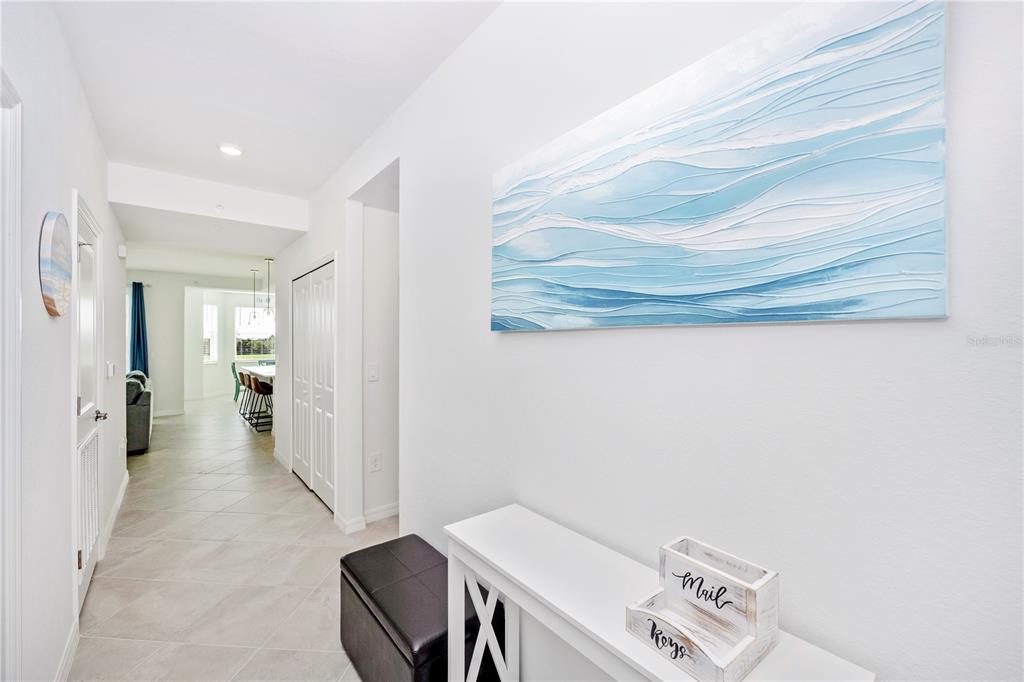 A hallway with light tile flooring leads toward an open kitchen area past a console table — 17565 OPAL SAND DRIVE UNIT 202, VENICE, FL