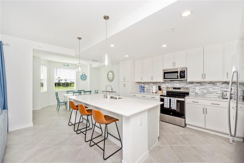 A modern kitchen features white cabinetry, a large quartz island with bar stools, and tile flooring — 17565 OPAL SAND DRIVE UNIT 202, VENICE, FL