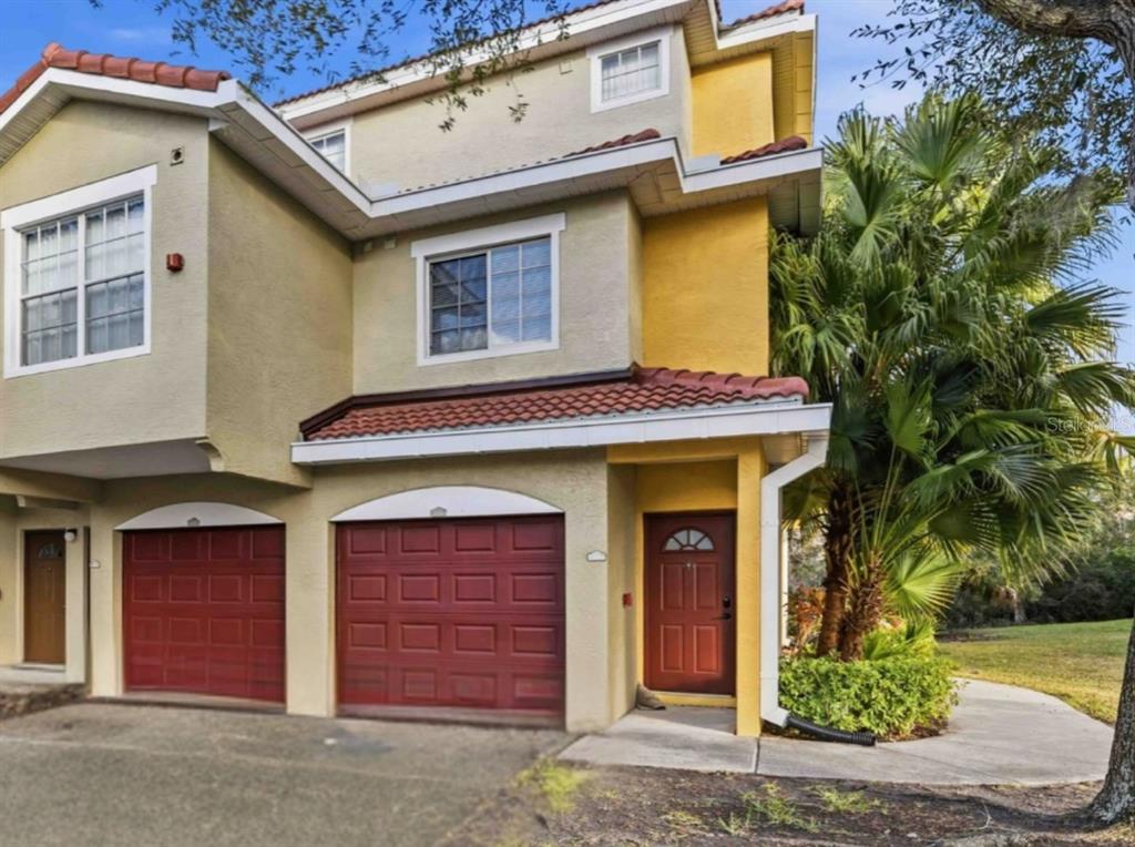A two-story townhouse exterior with a red tile roof, two garage doors, and a front entrance — 5721 BENTGRASS DRIVE UNIT 20-104, SARASOTA, FL