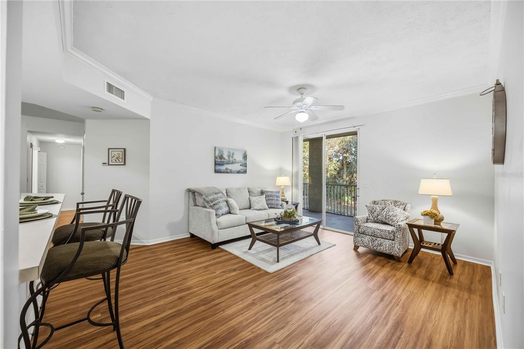 A living room features wood-look flooring, a sofa, an armchair, and a sliding glass door — 5721 BENTGRASS DRIVE UNIT 20-104, SARASOTA, FL