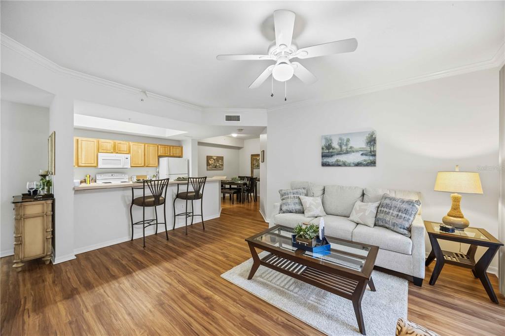 A living room with wood-look flooring, a ceiling fan, and an open kitchen with bar seating — 5721 BENTGRASS DRIVE UNIT 20-104, SARASOTA, FL