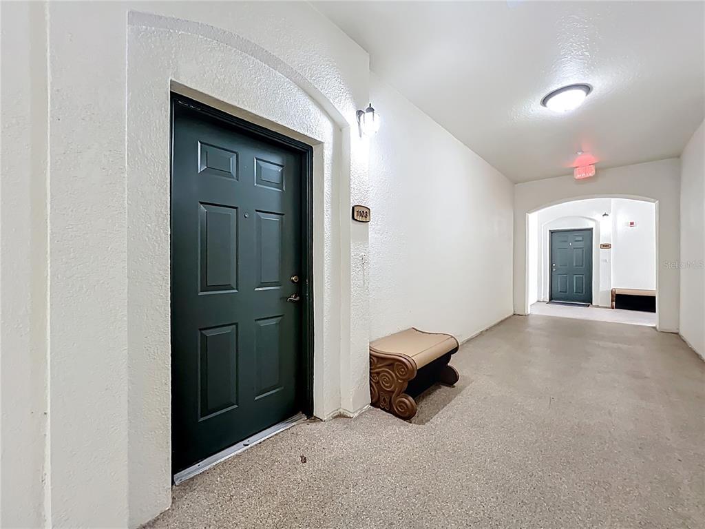 A dark green door with a small bench sits in a white apartment hallway — 11434 JASPER KAY TERRACE UNIT 106, WINDERMERE, FL