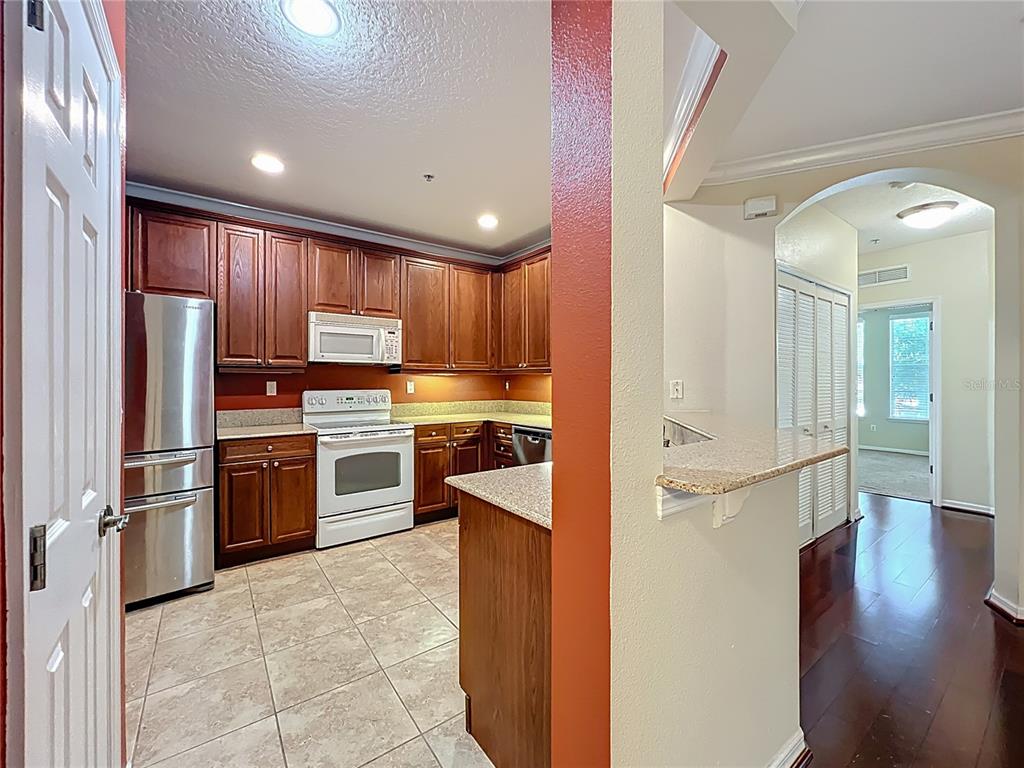 A kitchen with wood cabinets, stainless steel appliances, and tile flooring, viewed from an entryway — 11434 JASPER KAY TERRACE UNIT 106, WINDERMERE, FL
