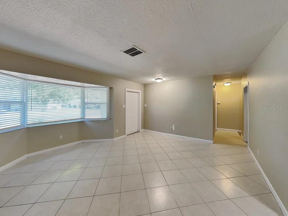 An empty room with light-colored tile flooring, beige walls, and a large bay window — 122 VAN DYCK DRIVE, NOKOMIS, FL