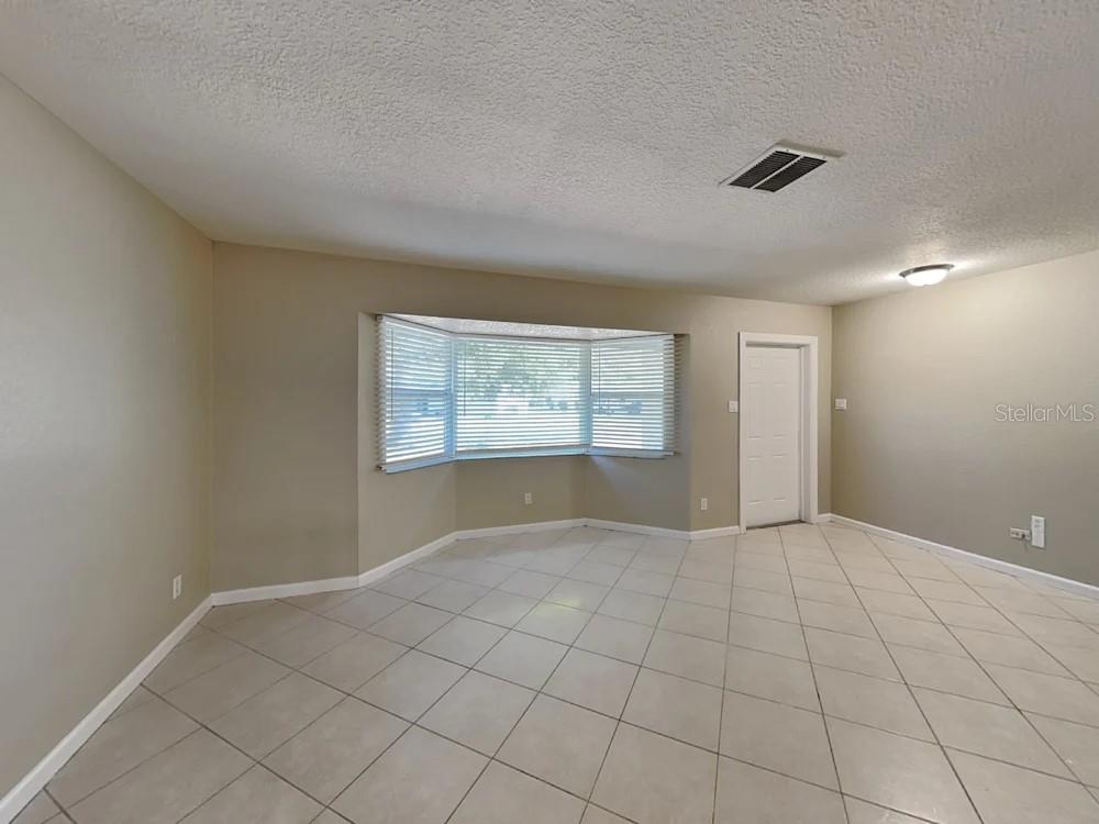 An empty room with beige walls, light-colored tile flooring, and a large bay window — 122 VAN DYCK DRIVE, NOKOMIS, FL