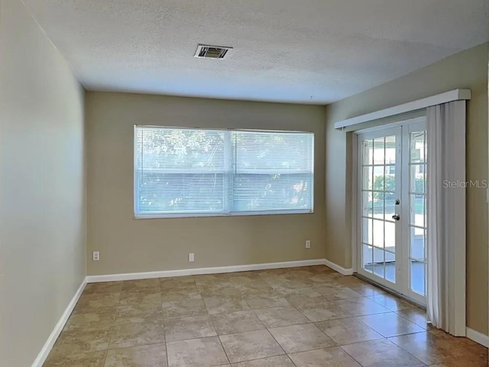 An empty room with tan walls, tile flooring, a large window, and glass patio doors — 122 VAN DYCK DRIVE, NOKOMIS, FL