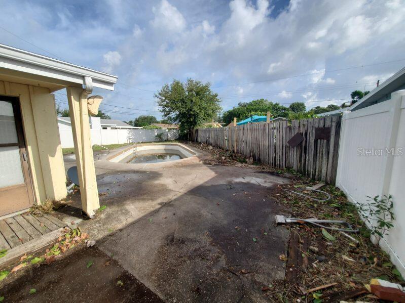 A backyard features a concrete patio, an empty swimming pool, and a wooden fence — 9956 136TH STREET, SEMINOLE, FL