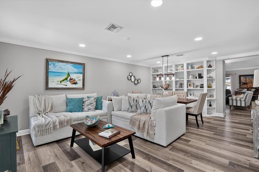 A living room features light gray walls, wood-look flooring, a sectional sofa, and built-in shelving — 24496 PEPPERCORN ROAD, PUNTA GORDA, FL