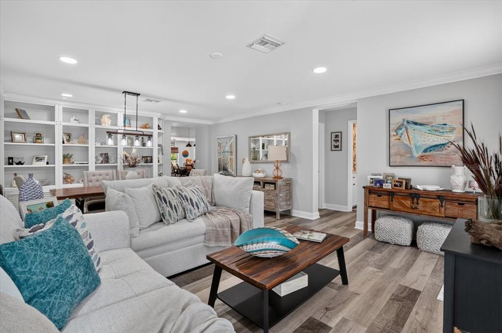 A living room features light gray walls, wood-look flooring, a sectional sofa, and built-in shelving — 24496 PEPPERCORN ROAD, PUNTA GORDA, FL