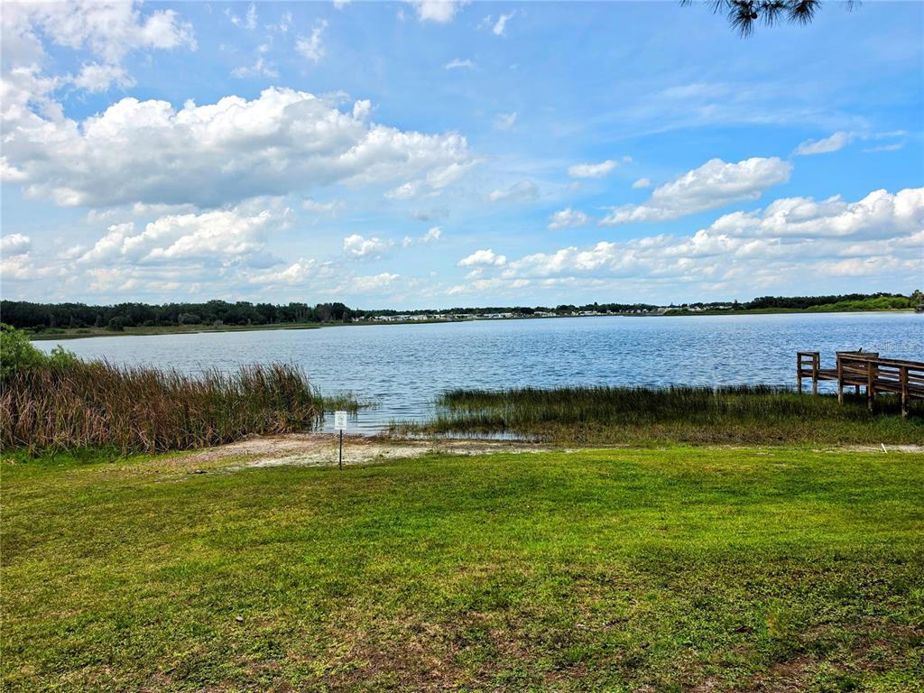 A grassy lawn leads to a lake with a wooden dock and tall reeds — 7336 INTERNATIONAL CIRCLE, LAKE WALES, FL