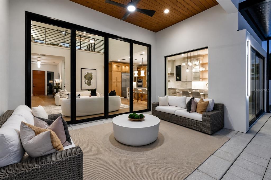 A covered outdoor patio features wicker sofas, a round coffee table, and large glass doors — 2121 CLEMATIS COURT, SARASOTA, FL