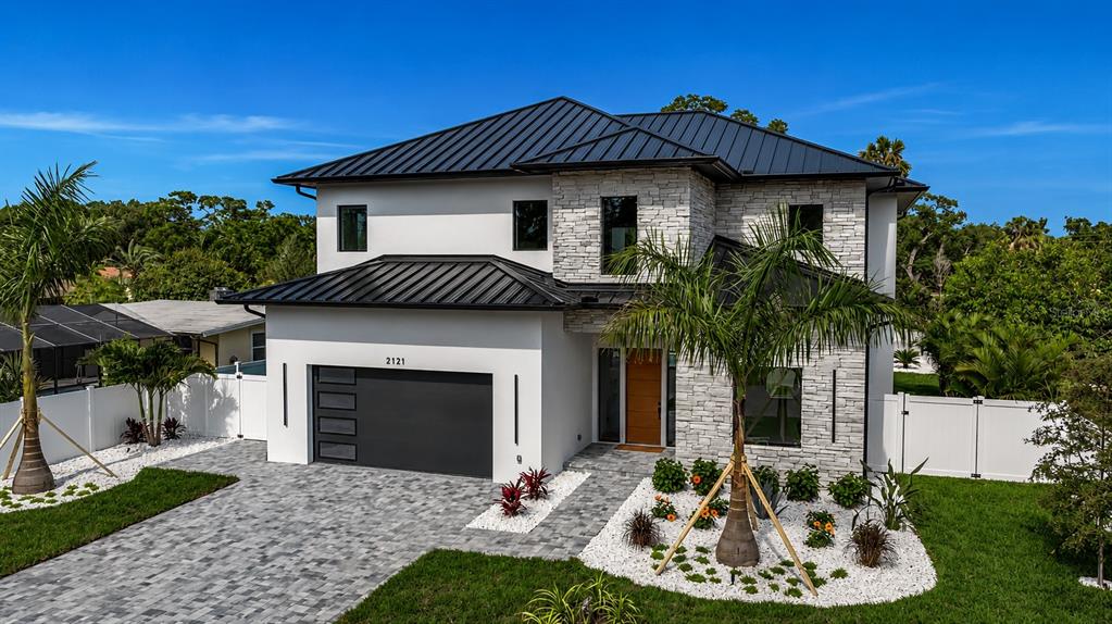 A two-story modern house features a white stucco exterior, stone accents, and a metal roof — 2121 CLEMATIS COURT, SARASOTA, FL