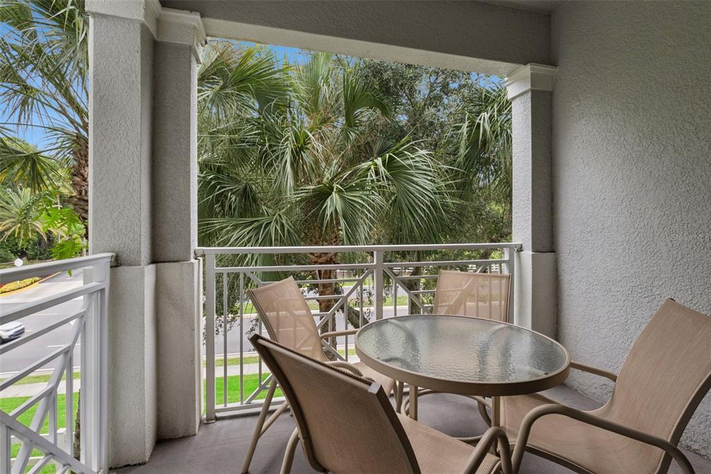 A covered balcony features a glass-topped table with four chairs overlooking palm trees and greenery — 5252 CANE ISLAND LOOP UNIT 204, KISSIMMEE, FL