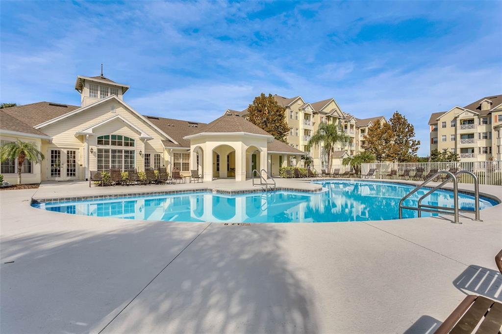 A swimming pool sits in front of a clubhouse and apartment buildings under a blue sky — 5252 CANE ISLAND LOOP UNIT 204, KISSIMMEE, FL
