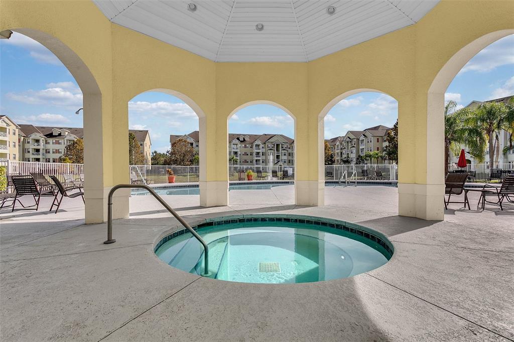A circular hot tub sits under a covered pavilion with arched openings overlooking an apartment complex — 5252 CANE ISLAND LOOP UNIT 204, KISSIMMEE, FL