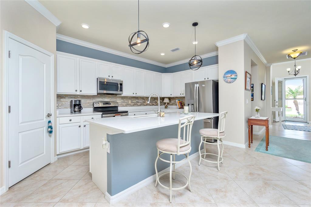A kitchen features white cabinets, a blue accent wall, a quartz island, and stainless appliances — 6139 GRAND CYPRESS BOULEVARD, NORTH PORT, FL
