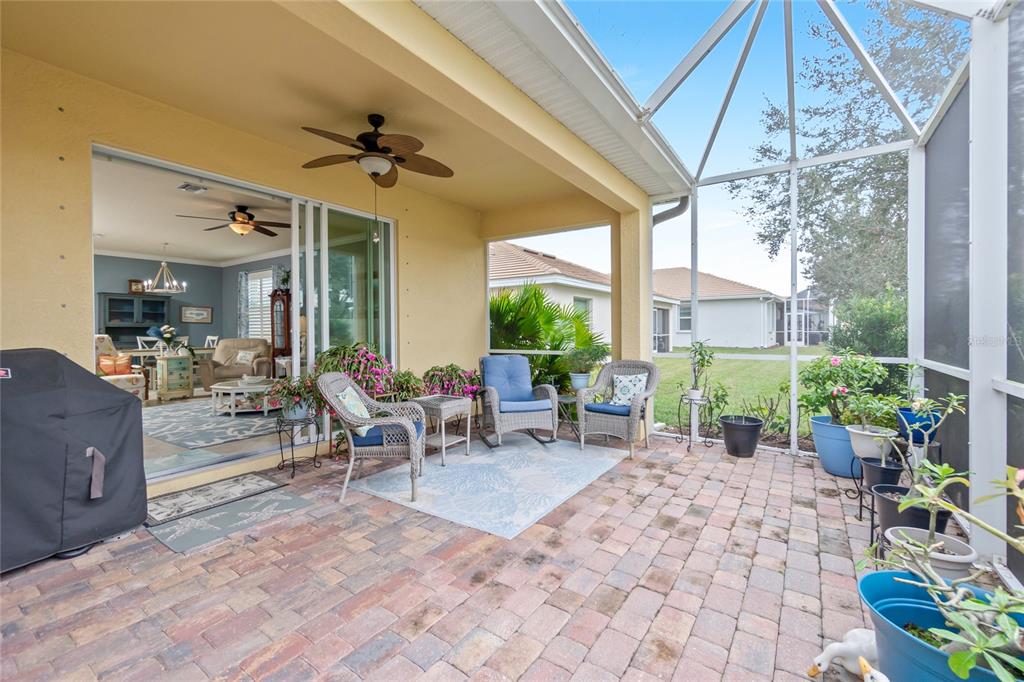 A covered patio with brick pavers, wicker furniture, and a screened-in enclosure overlooking a yard — 6139 GRAND CYPRESS BOULEVARD, NORTH PORT, FL