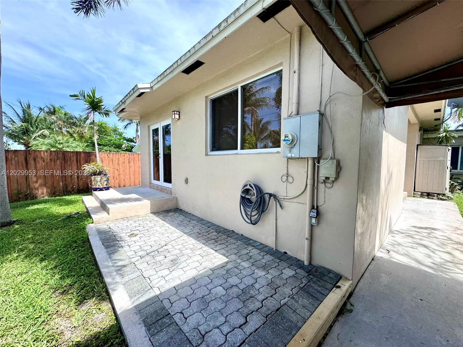 A beige house exterior features a paved patio, a sliding glass door, and a window — 1419 Garfield St, Hollywood FL 33020, HOLLYWOOD, FL