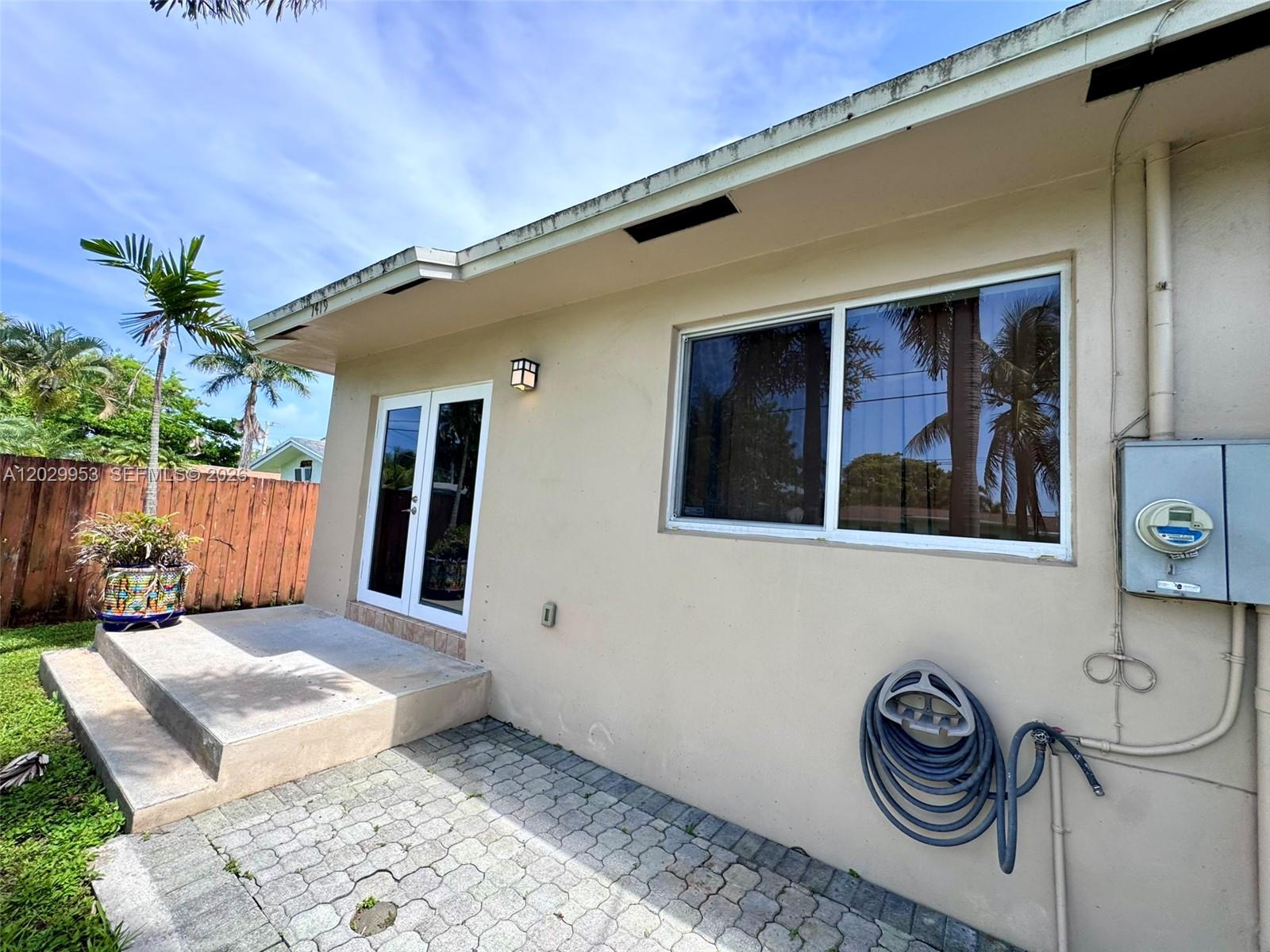 The exterior of a beige house features a concrete patio, French doors, and a window — 1419 Garfield St, Hollywood FL 33020, HOLLYWOOD, FL