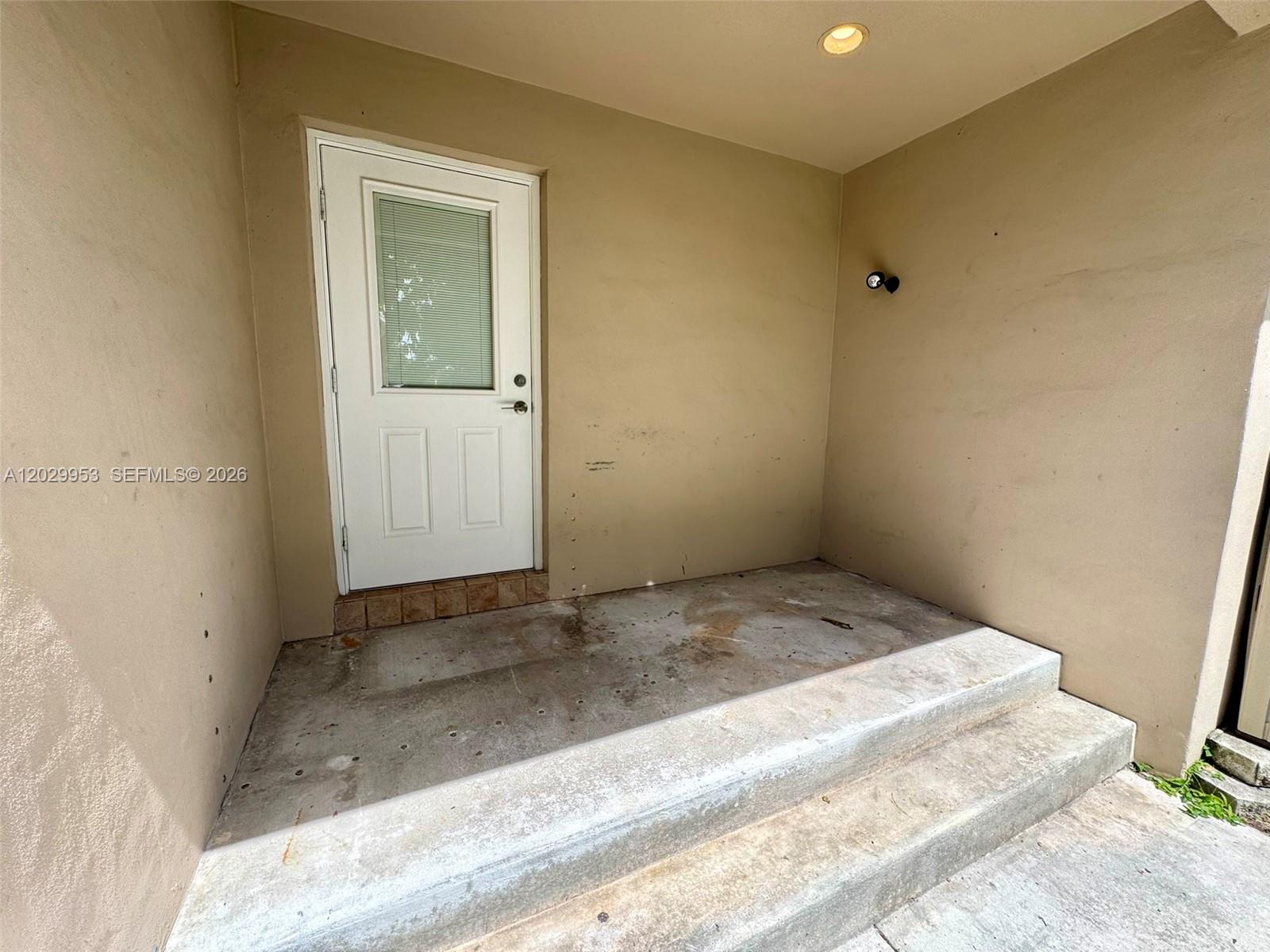 A concrete porch features a white door with a window and a single light fixture — 1419 Garfield St, Hollywood FL 33020, HOLLYWOOD, FL