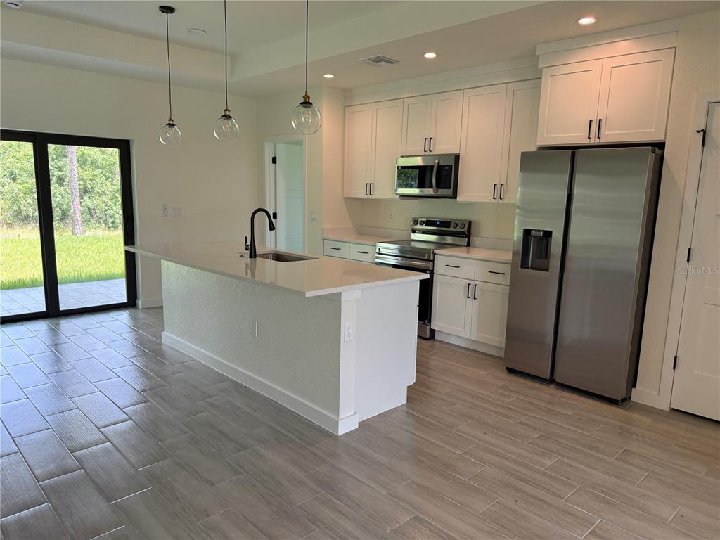 A modern kitchen features white cabinetry, stainless steel appliances, a center island, and tile flooring — 3764 CINDERELLA ROAD, NORTH PORT, FL