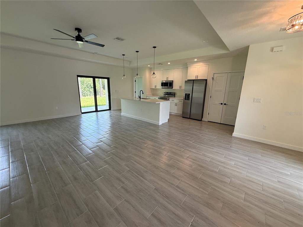 An open-concept kitchen and living area features light wood-look tile flooring and white cabinetry — 3764 CINDERELLA ROAD, NORTH PORT, FL