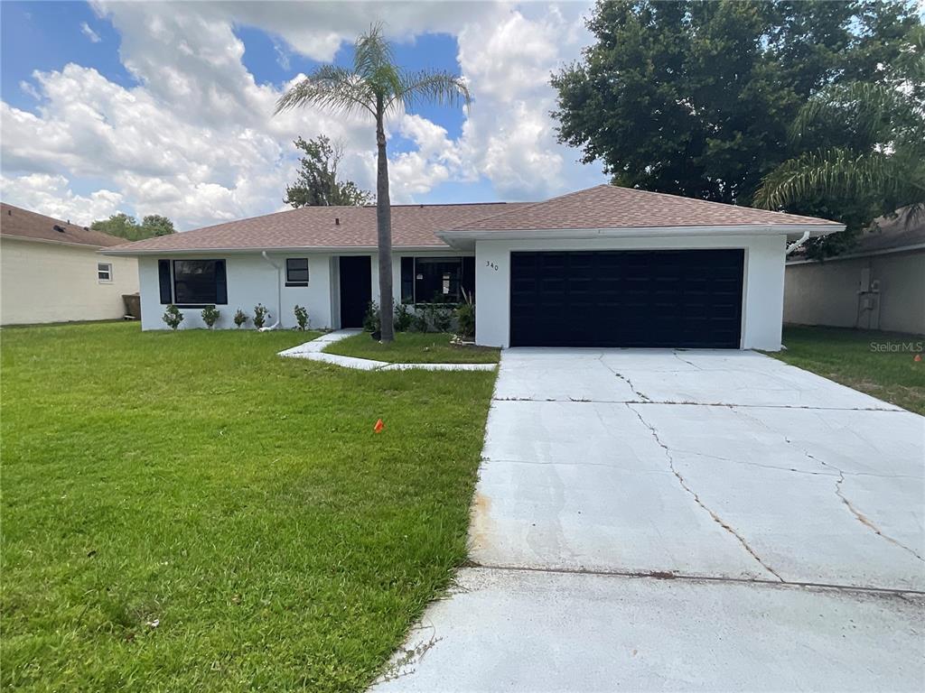 A single-story house with a white exterior, a black garage door, and a palm tree — 340 CHIQUITA COURT, KISSIMMEE, FL
