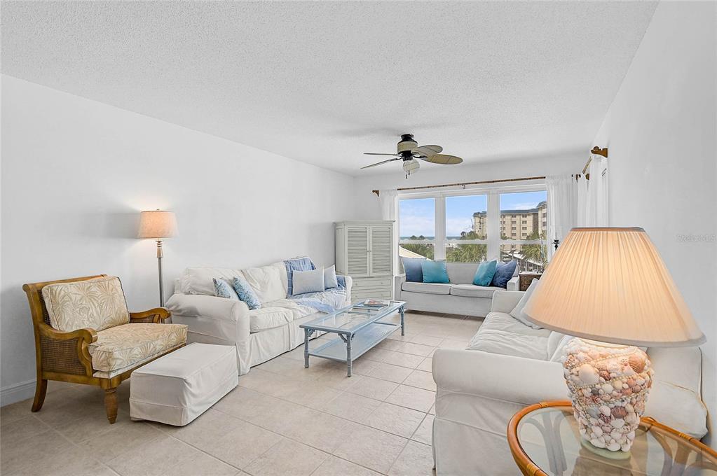 A bright living room features white sofas, a patterned armchair, and a view of the ocean — 845 BENJAMIN FRANKLIN DRIVE UNIT 402, SARASOTA, FL