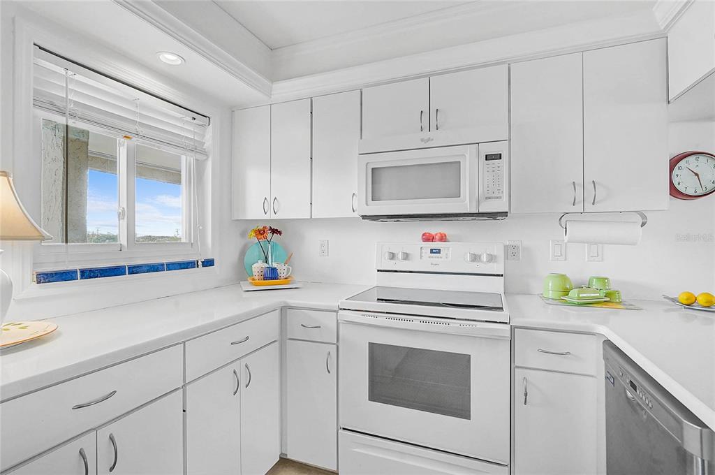 A white kitchen features white cabinets, white countertops, a white range, and a window — 845 BENJAMIN FRANKLIN DRIVE UNIT 402, SARASOTA, FL