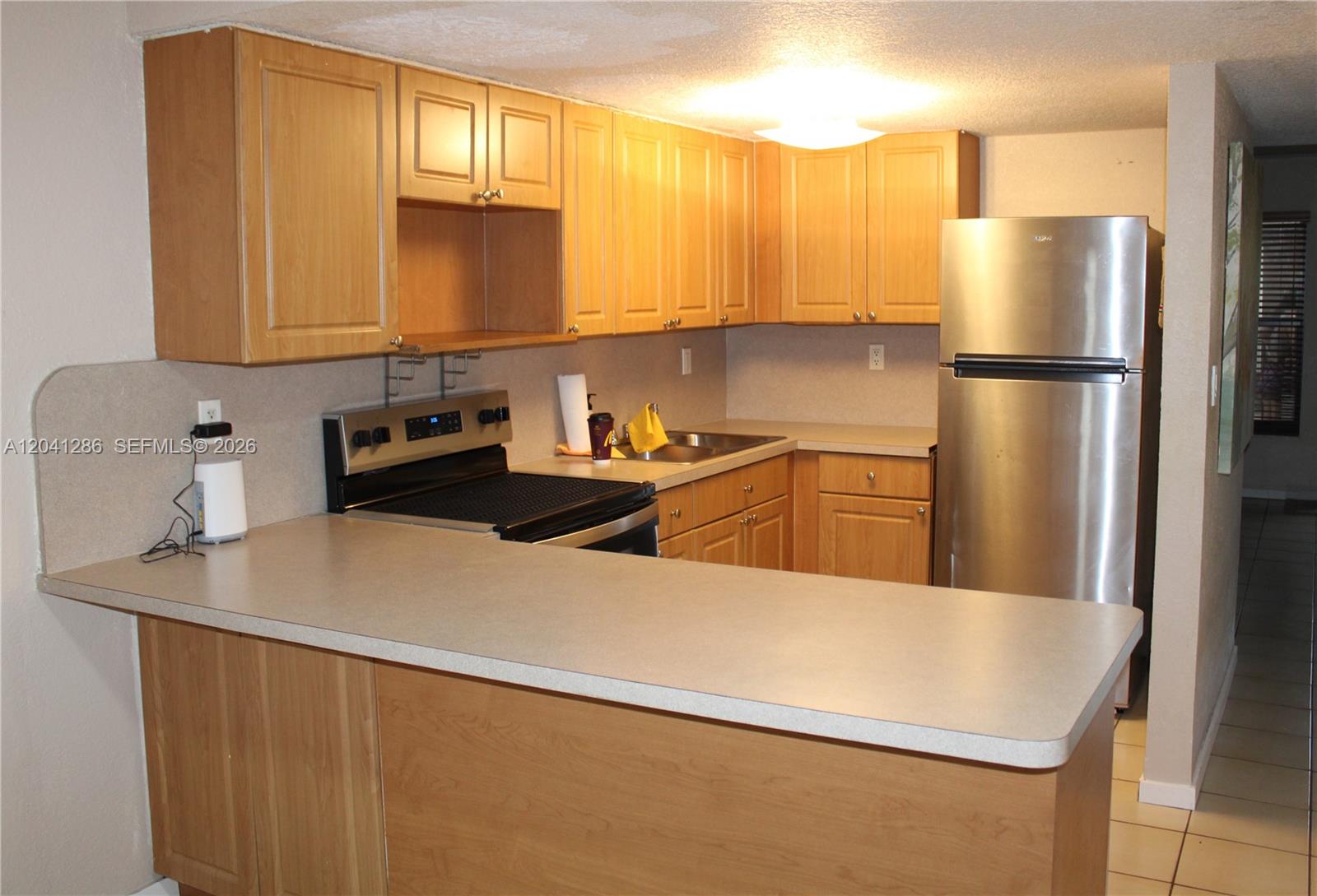 A kitchen features light wood cabinets, a stainless steel refrigerator, and a breakfast bar counter — 5446 W 26th Ave # 20, Hialeah FL 33016, HIALEAH, FL