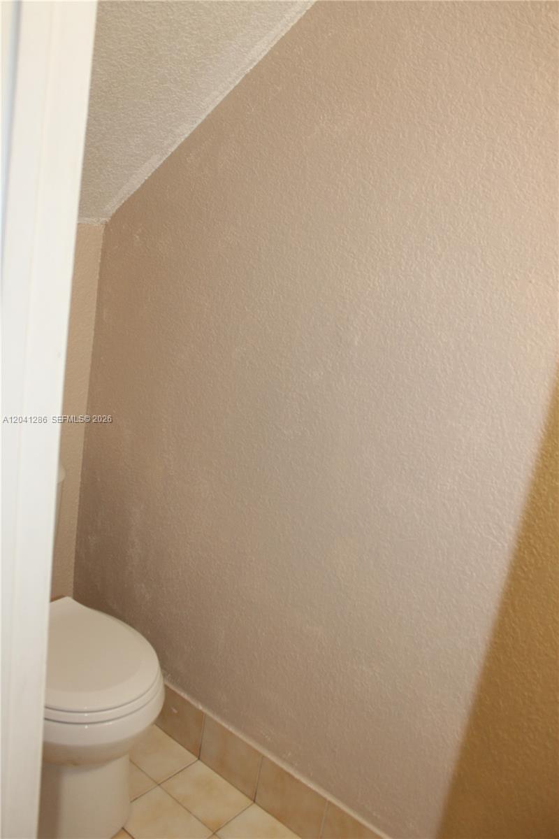 A white toilet sits in a small bathroom with beige walls and light-colored floor tiles — 5446 W 26th Ave # 20, Hialeah FL 33016, HIALEAH, FL