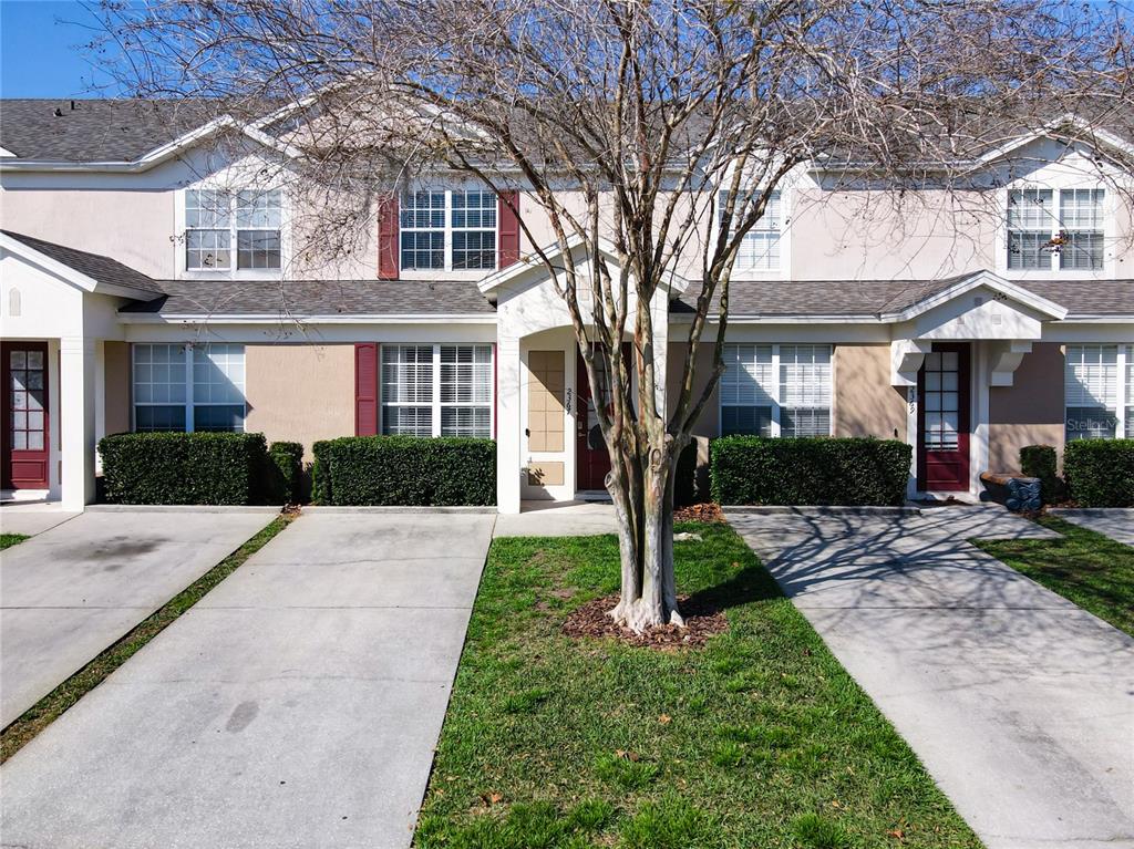 A row of three townhouses features beige stucco siding, red shutters, and individual concrete driveways — 2367 SILVER PALM DRIVE, KISSIMMEE, FL