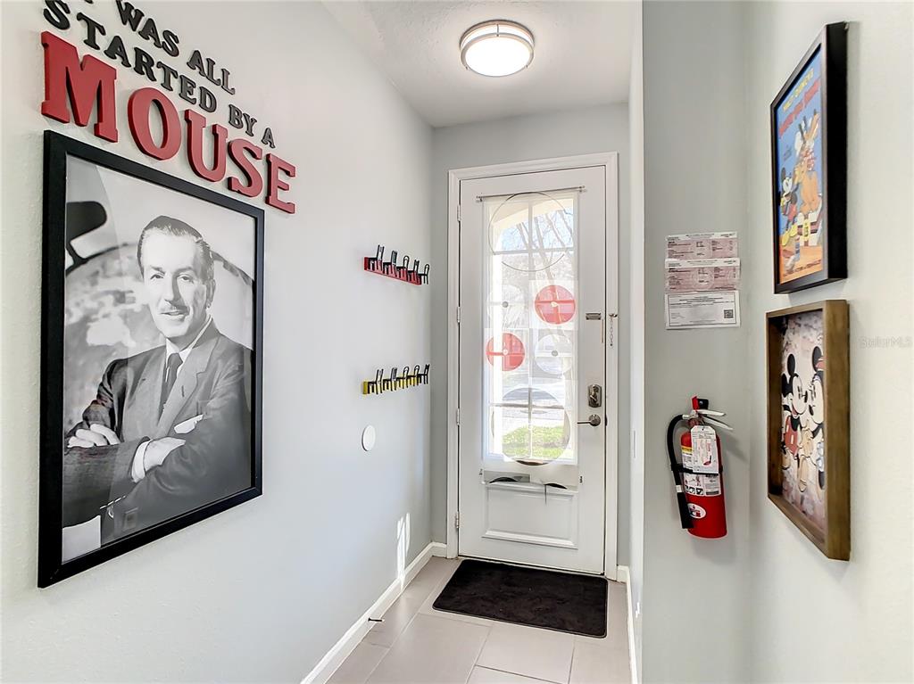 An entryway features Disney-themed wall art, a white front door, and a wall-mounted fire extinguisher — 2367 SILVER PALM DRIVE, KISSIMMEE, FL