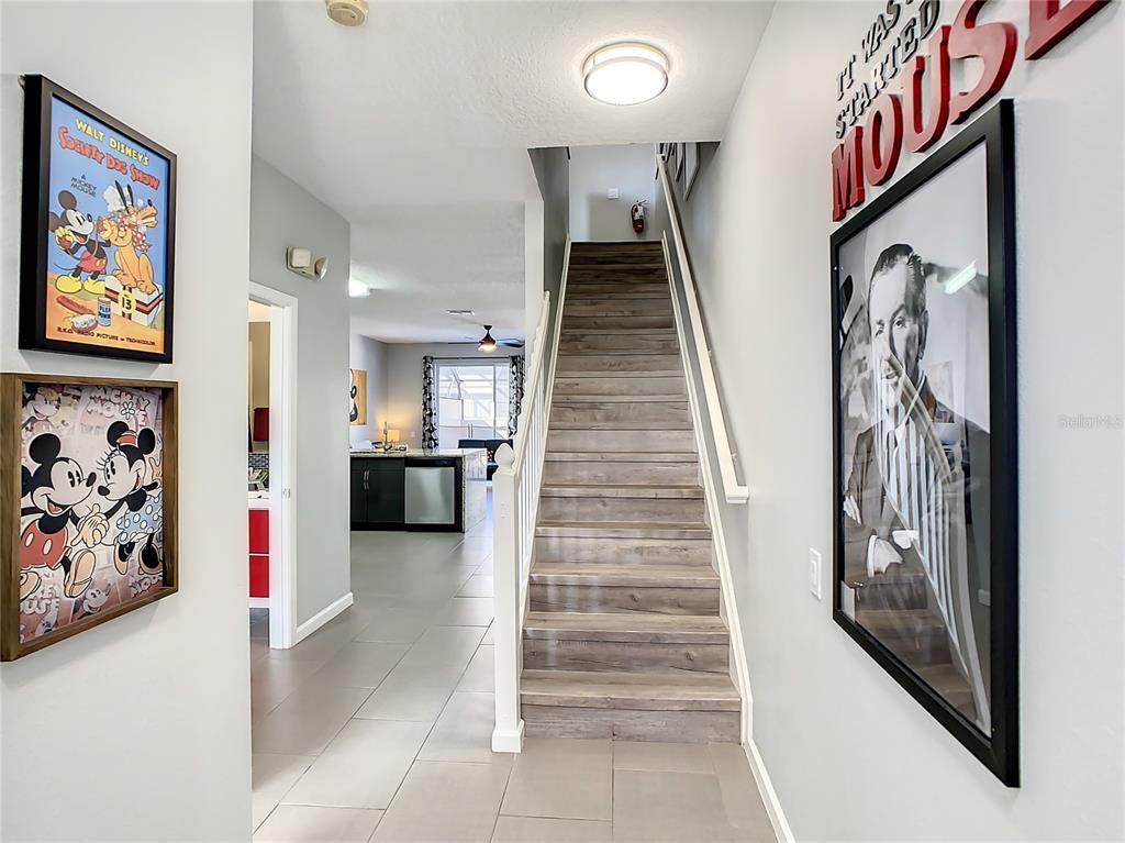 A staircase with wood-look steps leads upward between walls decorated with framed Disney artwork — 2367 SILVER PALM DRIVE, KISSIMMEE, FL