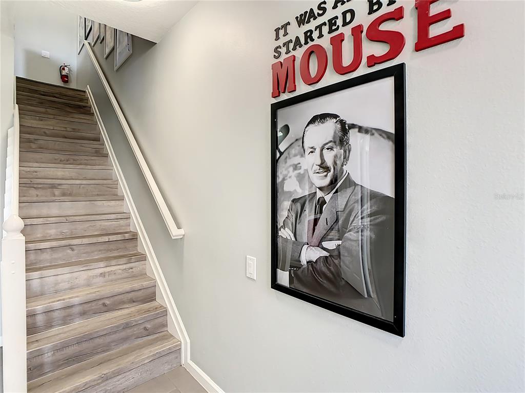 A staircase with wood-look steps sits beside a wall featuring a Walt Disney portrait — 2367 SILVER PALM DRIVE, KISSIMMEE, FL