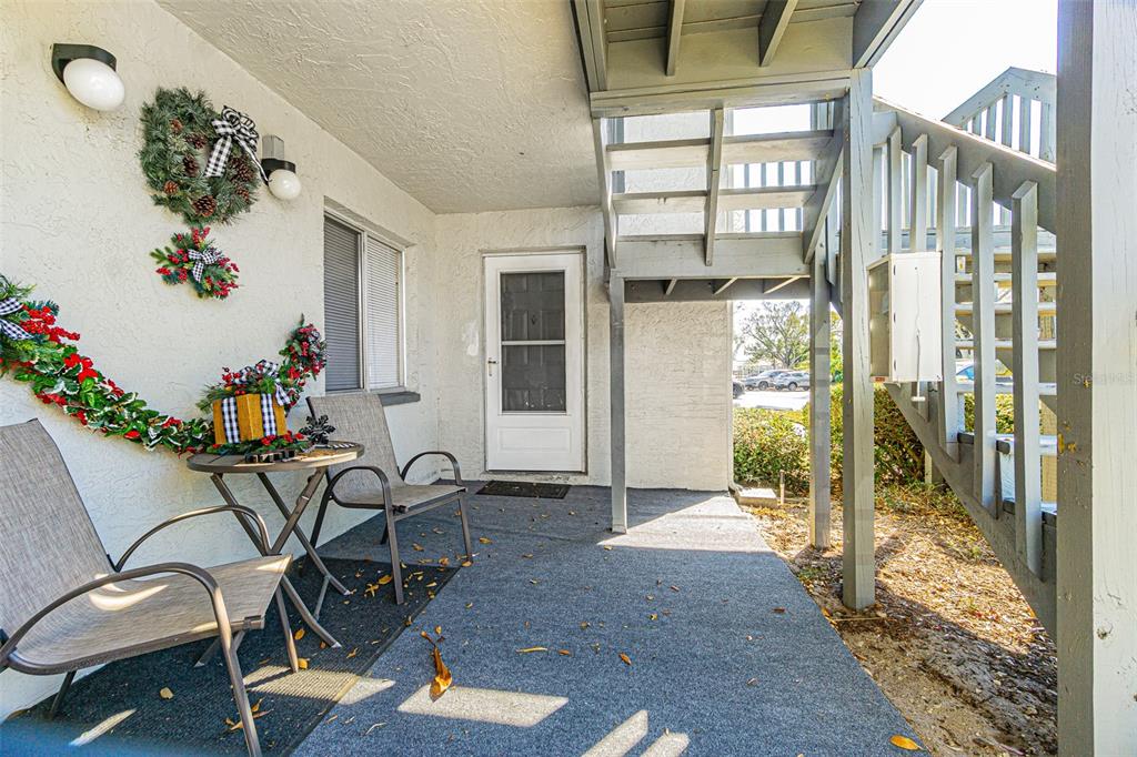 A covered patio features a small table, two chairs, holiday decorations, and an outdoor staircase — 11201 122ND AVENUE UNIT 197, LARGO, FL