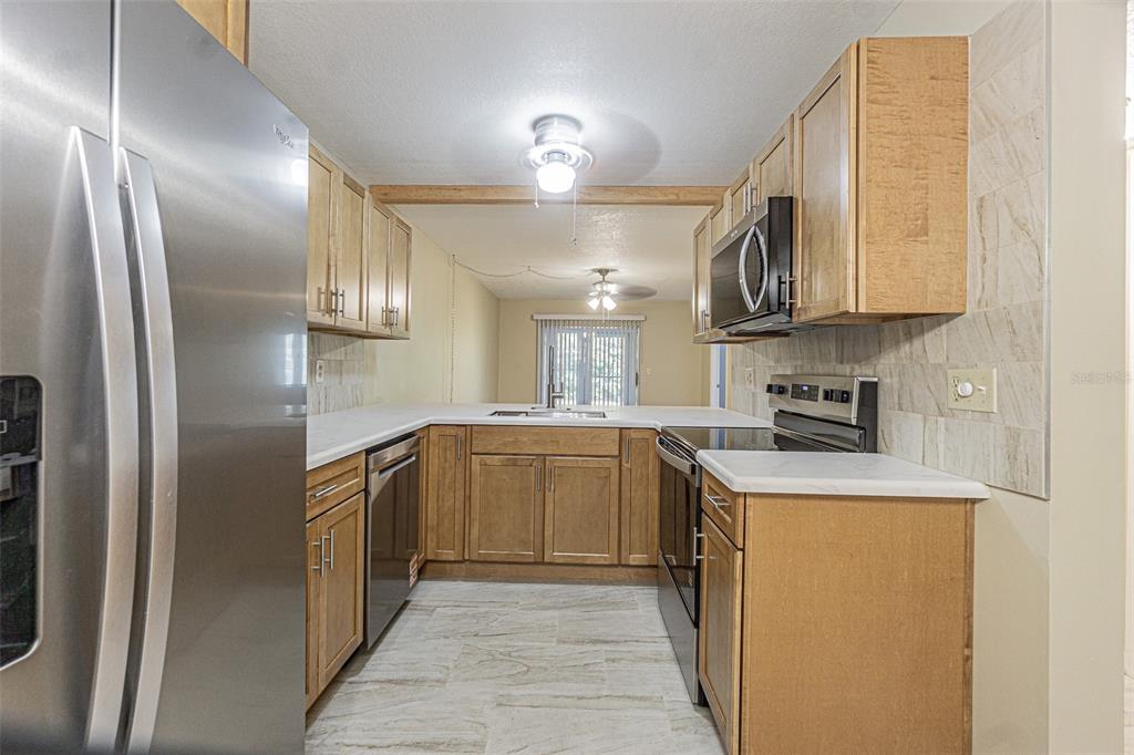 A kitchen with wood cabinets, white countertops, stainless steel appliances, and light-colored tile flooring — 11201 122ND AVENUE UNIT 197, LARGO, FL