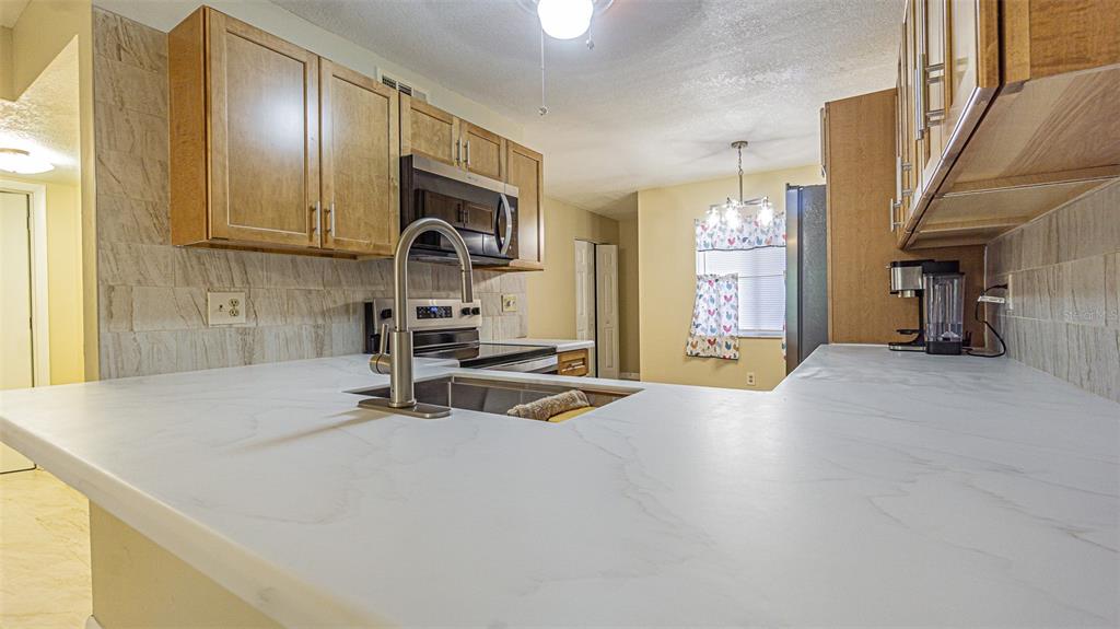A kitchen features light wood cabinets, white marble-look countertops, and a stainless steel sink — 11201 122ND AVENUE UNIT 197, LARGO, FL
