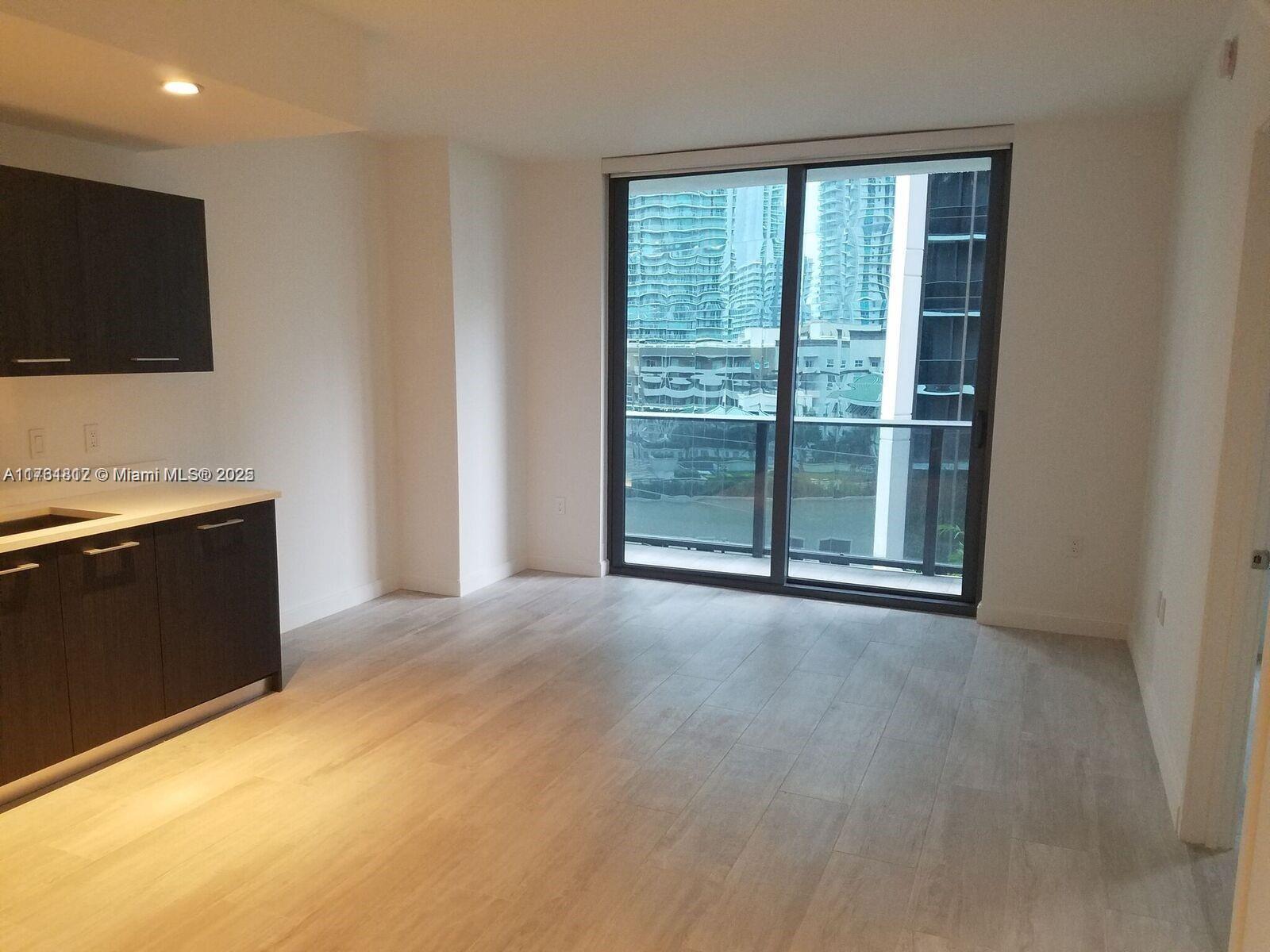 A kitchen area with dark cabinets and light wood floors opens to a balcony view — 55 SW 9th St # 1107, Miami FL 33130, MIAMI, FL