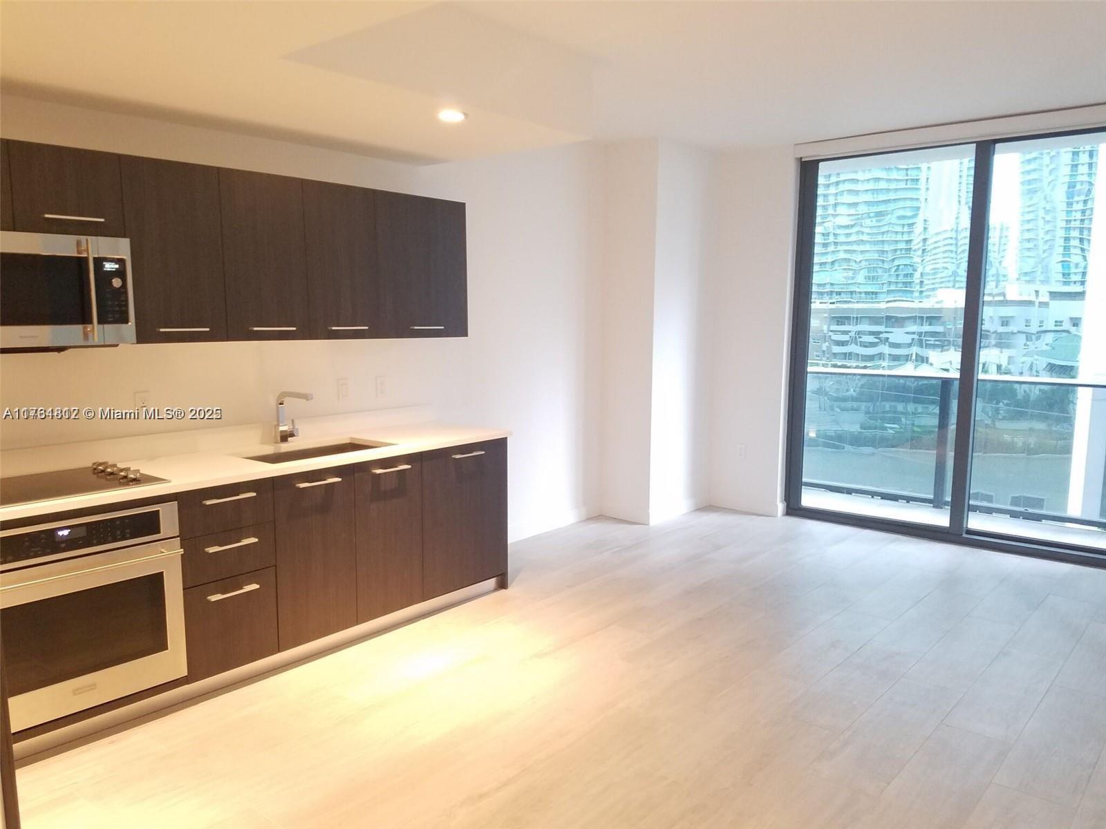A modern kitchen with dark wood cabinets and light flooring overlooks a city skyline — 55 SW 9th St # 1107, Miami FL 33130, MIAMI, FL