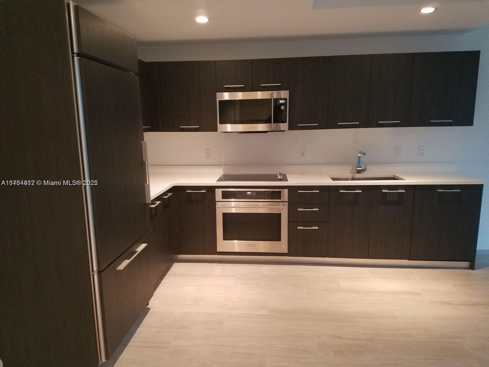 A modern kitchen features dark wood cabinetry, stainless steel appliances, and white countertops — 55 SW 9th St # 1107, Miami FL 33130, MIAMI, FL