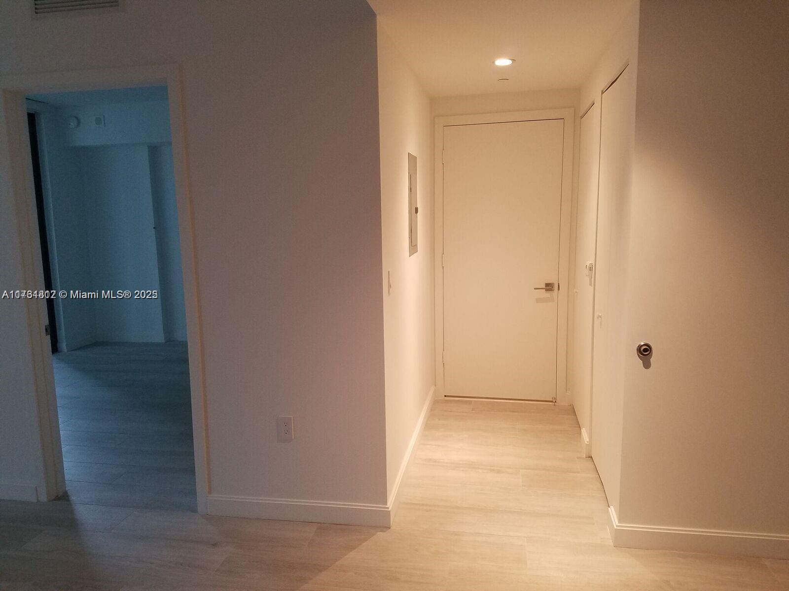 A hallway with light wood-look flooring leads to a closed white door — 55 SW 9th St # 1107, Miami FL 33130, MIAMI, FL
