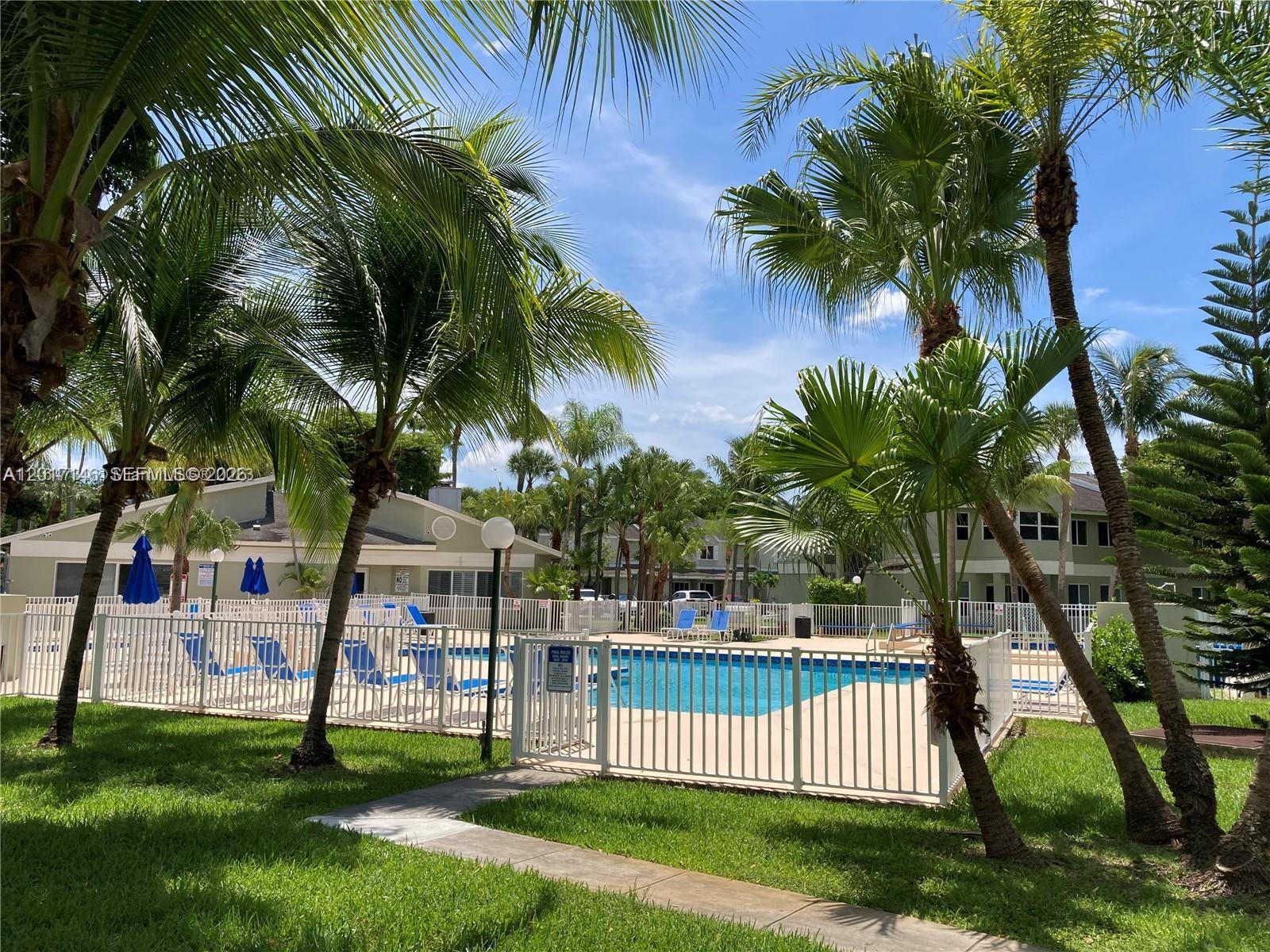 A swimming pool enclosed by a white fence is surrounded by palm trees and buildings — 6725 NW 174th Ter # 12, Hialeah FL 33015, HIALEAH, FL