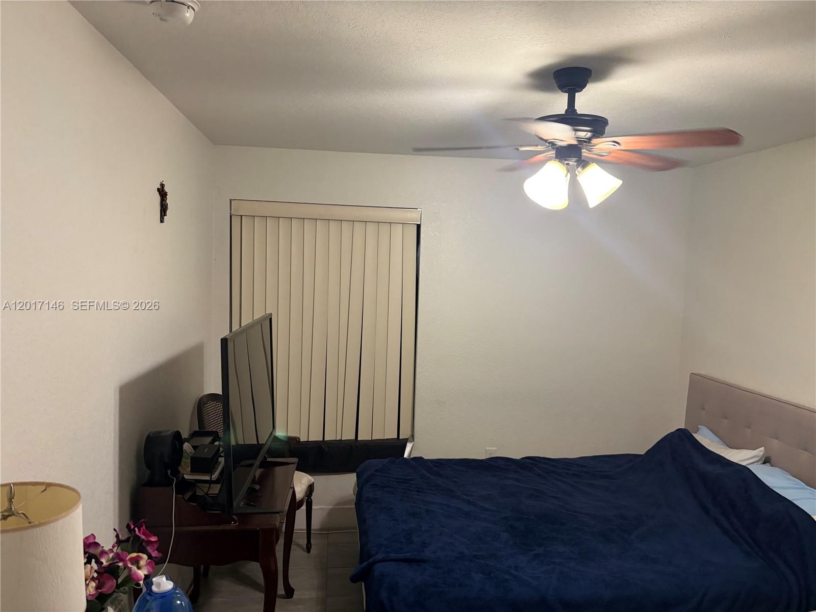 A bedroom features a bed with a blue blanket, a ceiling fan, and a television — 6725 NW 174th Ter # 12, Hialeah FL 33015, HIALEAH, FL