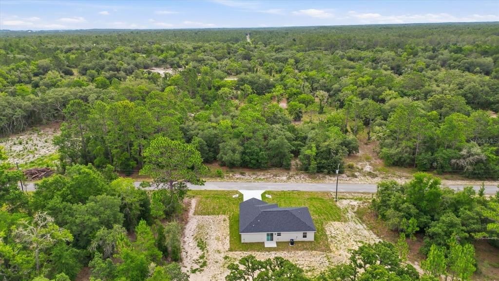 An aerial view shows a single-story house with a dark roof surrounded by wooded land — 0000 SW SANDS PT AVE LOT 32, DUNNELLON, FL
