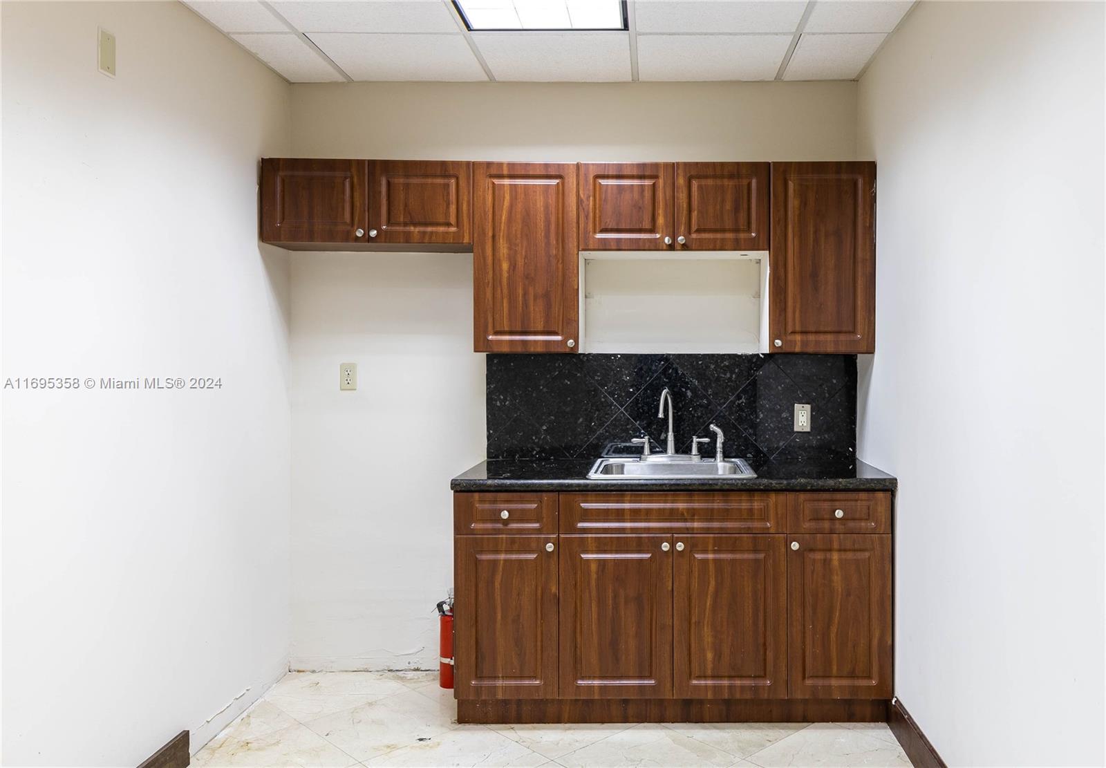 A small kitchenette features dark wood cabinets, a black granite countertop, and a stainless sink — 2500 E Hallandale Beach Blvd, Hallandale Beach FL 33009, HALLANDALE BEACH, FL