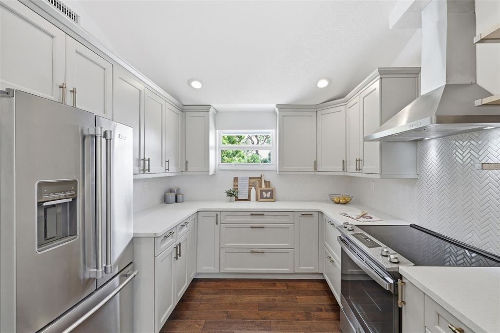 A modern kitchen features light gray cabinets, white countertops, stainless steel appliances, and wood flooring — 7 GEORGIA AVENUE, CRYSTAL BEACH, FL